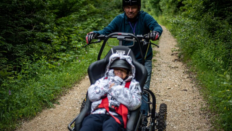 _DSC5752 Alan Manzanedo poussant un vélo-fauteuil sur un chemin en forêt